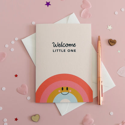Greeting card with rainbow design and 'Welcome Little One' text on a pink background with confetti.